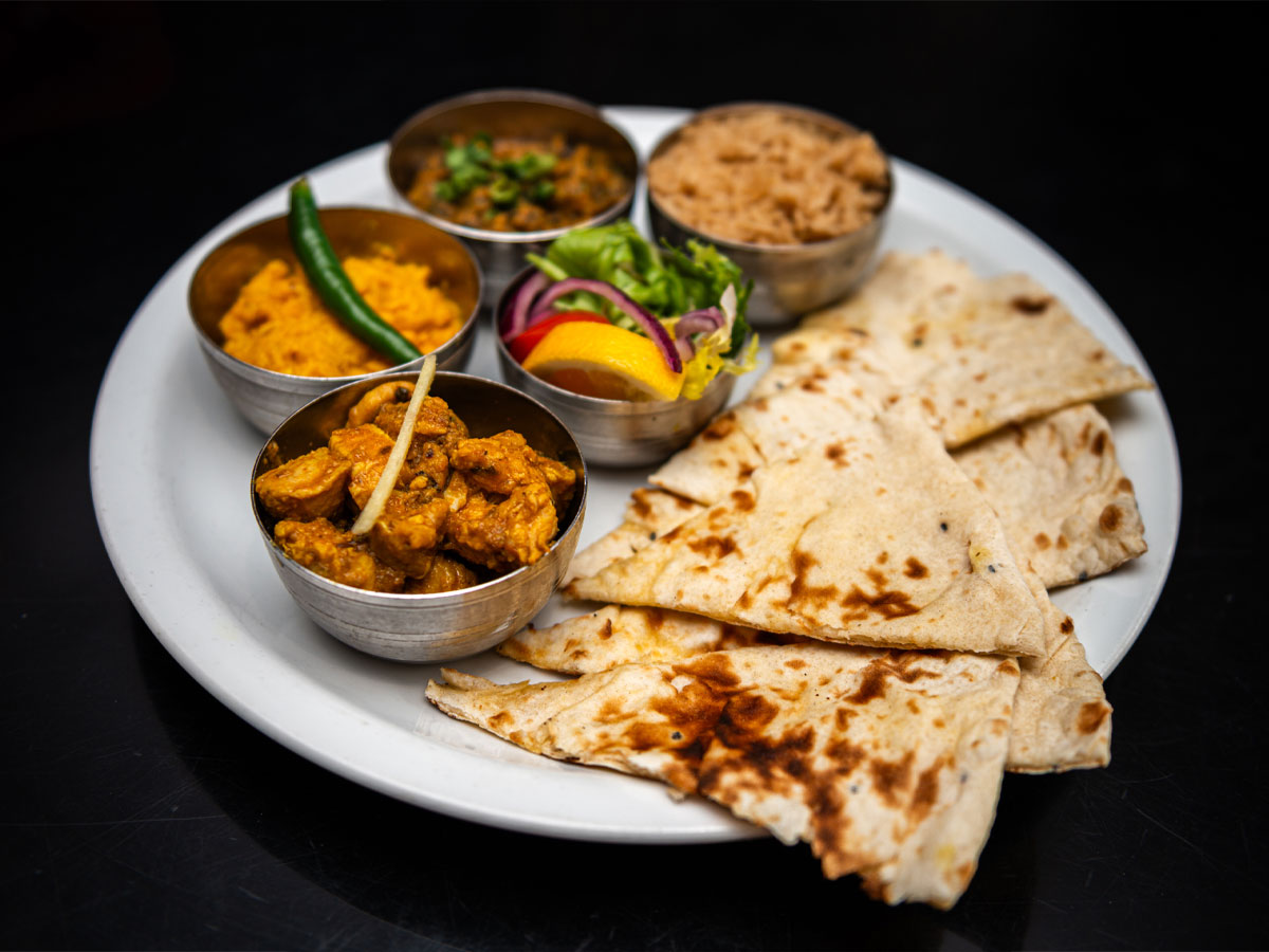 Photography of mixed curries in dishes with naan bread on a plate